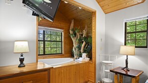 Un bagno in legno con vasca, mobile lavabo in legno, lavandino e una finestra vista alberi.