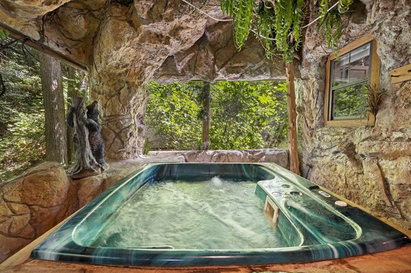 A hot tub in a natural stone setting with a view of trees.