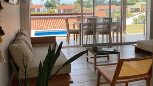 A spacious living room with a wooden ceiling, a large sliding glass door leading to an outdoor patio, and a view of a swimming pool and neighboring houses. - Tres Colinas Estancia 27 (Armenia)
