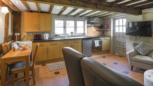 A kitchen with wooden beams, a dining table with chairs, a sofa, and a TV mounted on the wall. - A relaxing escape for couples in a cosy old cottage with gorgeous rural views. (Llangollen)
