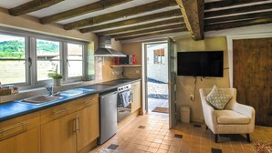 A kitchen with wooden beams, a built-in oven, a sink, and a television mounted on the wall. - A relaxing escape for couples in a cosy old cottage with gorgeous rural views. (Llangollen)