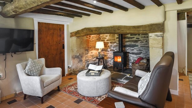 A cozy living room with a stone fireplace, wooden beams, a television, and comfortable seating. - A relaxing escape for couples in a cosy old cottage with gorgeous rural views. (Llangollen)