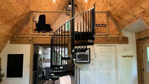 A spacious loft-style living area with a wooden ceiling, a spiral staircase, a kitchen, and a cozy seating area.