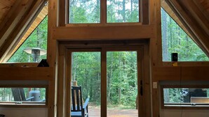 A wooden cabin with a large central door and two side windows, offering views of a forested area.