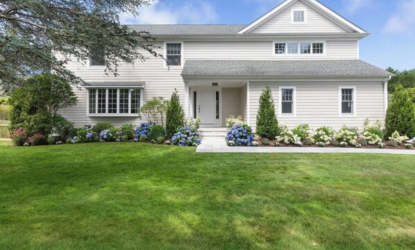 A two-story house with a front porch, a well-maintained lawn, and a variety of flowering plants.