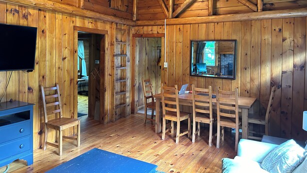 L’intérieur d  ’un chalet en bois est aménagé avec un téléviseur, des chaises en bois, une table à manger et un miroir qui reflète l’extérieur.