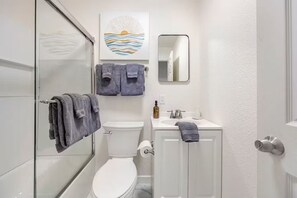 Un baño moderno con cabina de ducha de vidrio, inodoro, lavamanos con espejo y dos toallas colgadas en la pared.