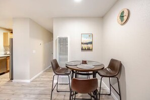 Un comedor con una mesa redonda, cuatro sillas, un reloj y una ventana con persianas.