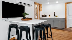 Una cocina moderna con encimera blanca, taburetes negros, un macetero de madera y armarios grises.
