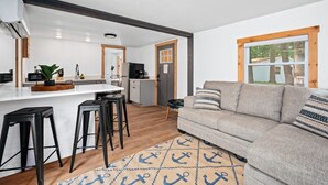 Una cocina moderna con una isla central, taburetes de bar, un sofá gris y una alfombra con motivos náuticos.