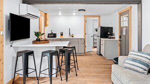 Una cocina moderna con una televisión de pantalla plana, un microondas y una cafetera. Hay tres taburetes y un sofá con un cojín estampado.