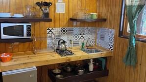 Eine kleine Küche mit Holzvertäfelung, einer Mikrowelle, einem kleinen Kühlschrank, einem Spülbecken und einem Herd.