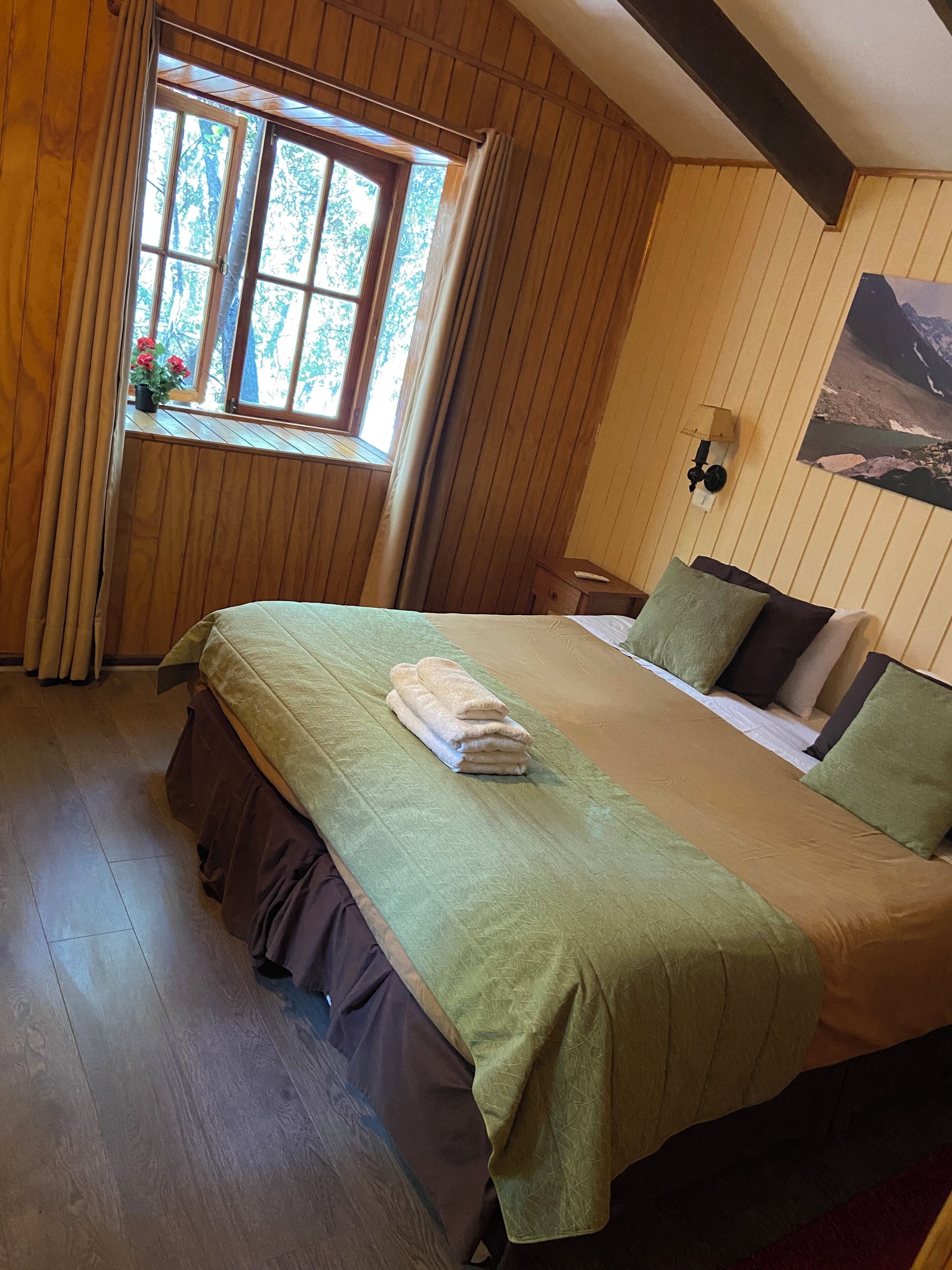 Une chambre avec un grand lit, des murs en bois, une fenêtre avec des rideaux et une lampe fixée au mur.