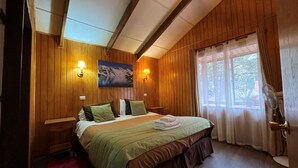 Ein Schlafzimmer mit Holzwänden, einem Bett, zwei Nachttischen, einer Wandlampe, einem Gemälde und einem Fenster mit Vorhängen.
