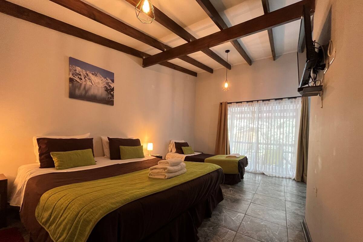Una camera d'albergo con due letti, un quadro, una finestra con tende e un pavimento piastrellato.