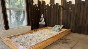 Ein Meditationsbereich mit einer Holzplattform, die mit weißen Kieselsteinen gefüllt ist, einem Kissen und einer Buddha-Statue.