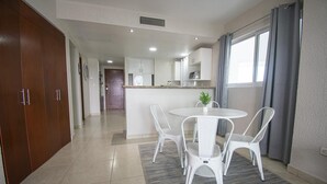 Una cocina moderna con armarios blancos, una isla central y un comedor con sillas y mesa blancos.