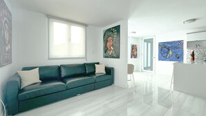 A modern living room with a teal sofa, a dining area with a table and chairs, and a kitchen with a white countertop and a decorative item. - New Boutique House with Pool near the Beach (Rincón)