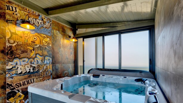 Un jacuzzi dans une pièce dont un mur est recouvert de graffitis et qui possède de grandes fenêtres.