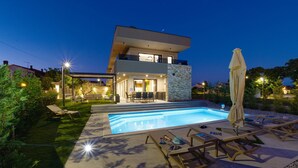 Une maison moderne à deux étages, dotée d’une piscine, d’un espace extérieur aménagé et d’un patio bien éclairé.