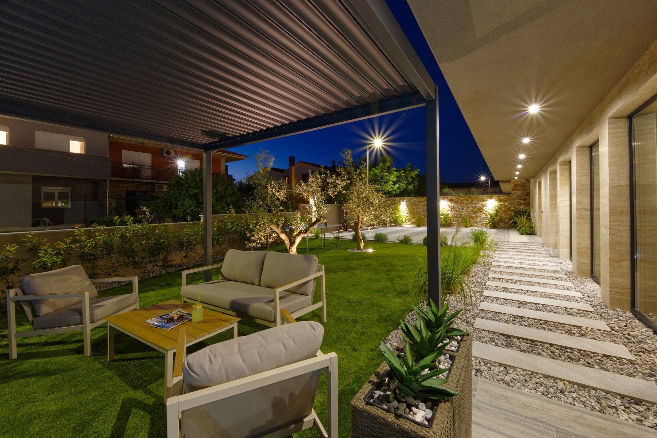 An outdoor patio area with a covered seating area, a pathway, and a well-maintained lawn.