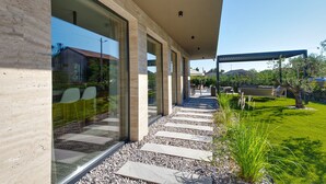 Un bâtiment moderne doté d’un espace extérieur couvert, d’un escalier en pierre et d’un jardin verdoyant.