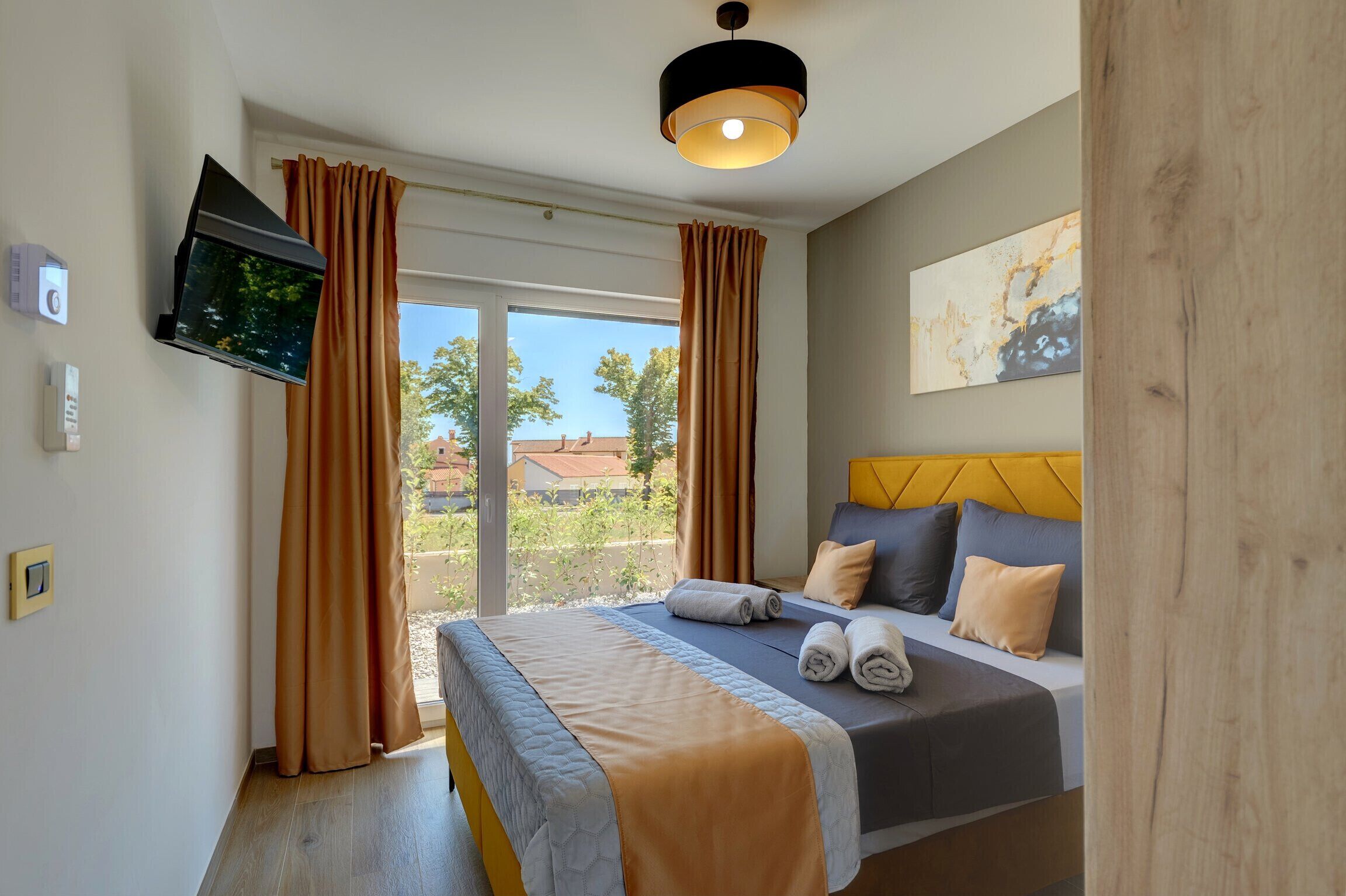 Une chambre d’hôtel avec un lit, un téléviseur fixé au mur et une fenêtre avec des rideaux.