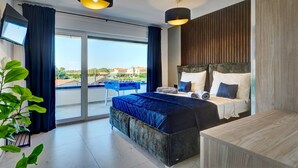 Une chambre moderne avec un grand lit, un téléviseur fixé au mur, un balcon avec une table et une vue sur les bâtiments environnants.