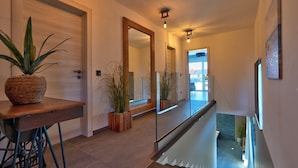 A modern hallway with a wooden desk, potted plants, and a glass railing overlooking a lower level. - Villa Bavigo - Luxury Spa Oasis (Marcana)