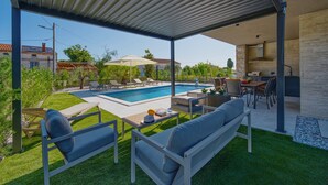 A covered outdoor area with a pool, seating, and a kitchen area. - Villa Bavigo - Luxury Spa Oasis (Marcana)