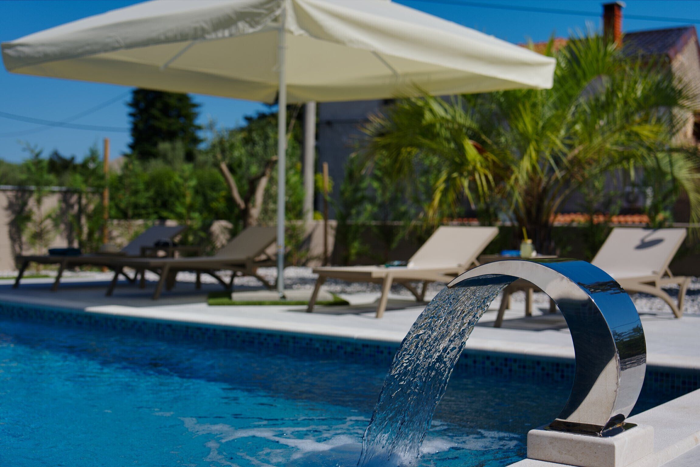 A swimming pool with a water feature, lounge chairs, and an umbrella.
