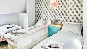 A hotel room with two beds, a bedside table, a lamp, and a wall-mounted picture. - 5 bedroom accommodation in Grantham (Grantham)