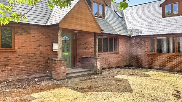 A brick building with a green door, a small porch, and a gravel yard. - 5 bedroom accommodation in Grantham (Grantham)