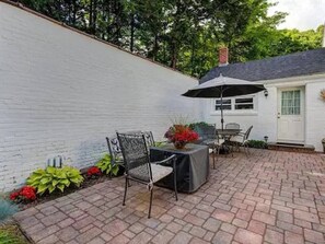 A patio with a white wall, a brick floor, and outdoor furniture including a table and chairs.