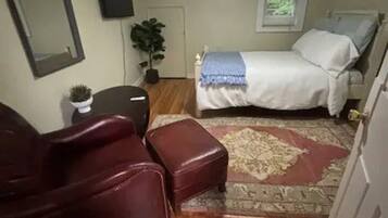 Een slaapkamer met een bed, een plafondventilator, een potplant, een spiegel en een rode leren fauteuil.