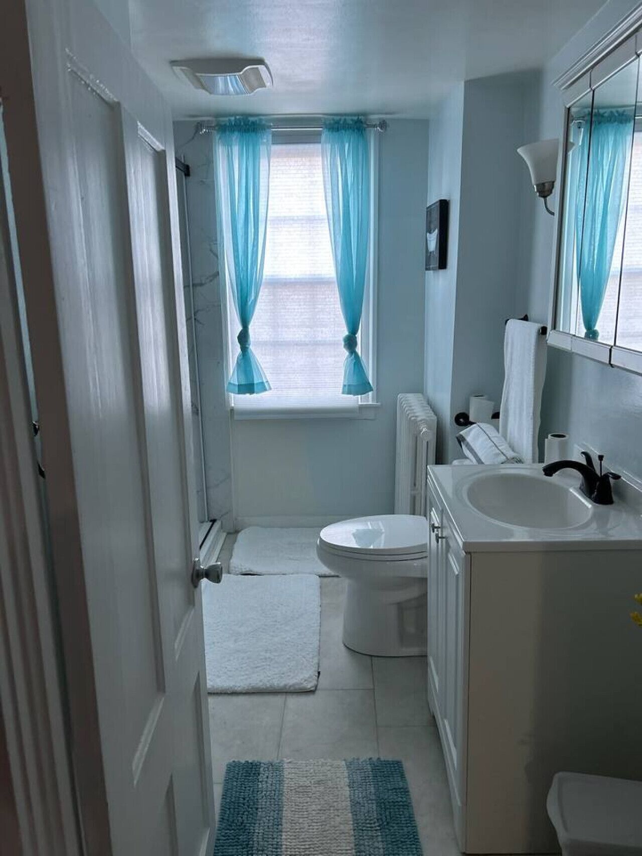 A compact bathroom with a toilet, sink, and window with curtains.