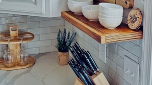 Una cocina con armarios blancos, repisas de madera que sostienen cuencos y una tabla de cortar, un organizador de cuchillos y una pequeña planta en maceta.