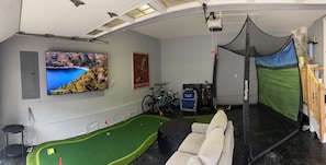 Ein Zimmer mit großem Fernseher, Golfwagen, Tennisnetz und einer Couch.
