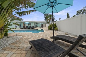 A backyard with a pool, lounge chairs, and umbrellas.