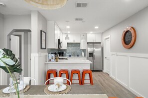A modern kitchen with white cabinets, a stainless steel refrigerator, and a central island with orange stools.