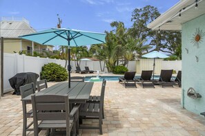 A backyard with a pool, outdoor furniture, and umbrellas.