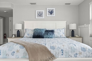 A bedroom with a bed, two bedside tables, a headboard, and two wall-mounted pictures.
