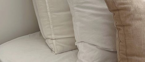 A bed with white bedding and a beige pillow.
