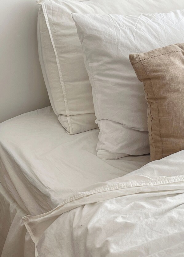 A bed with white bedding and a beige pillow.