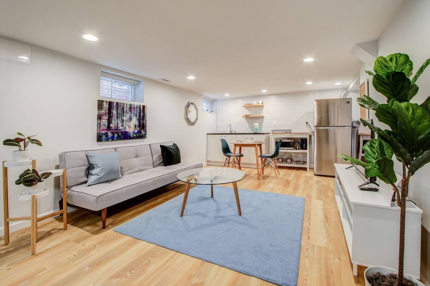 Un salon moderne avec un canapé, une table basse et un coin repas avec des chaises. On aperçoit au fond une cuisine équipée d’un réfrigérateur et d’un évier.