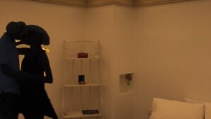 Una habitación con un techo alto y arqueado, y una cama blanca con almohadas. Hay un estante blanco con un objeto rojo encima.