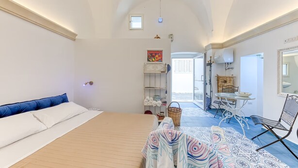 Un dormitorio con una cama, un escritorio y una silla. Hay una ventana y una puerta que conduce a otra habitación.