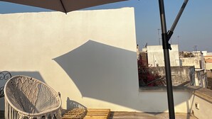 Una terraza en la azotea con un paraguas grande, una silla de mimbre y un trípode.