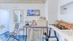 Cocina compacta con estufa a gas, lavamanos y comedor con una silla y mesa.