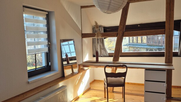 Un dormitorio con techo inclinado, un escritorio, una silla, un radiador y una ventana con persianas.